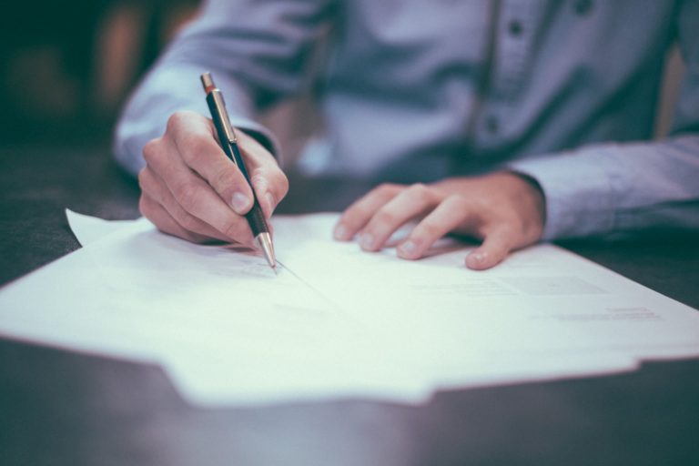 A businessman writing on paper. Photo source: Scott Graham via Unsplash