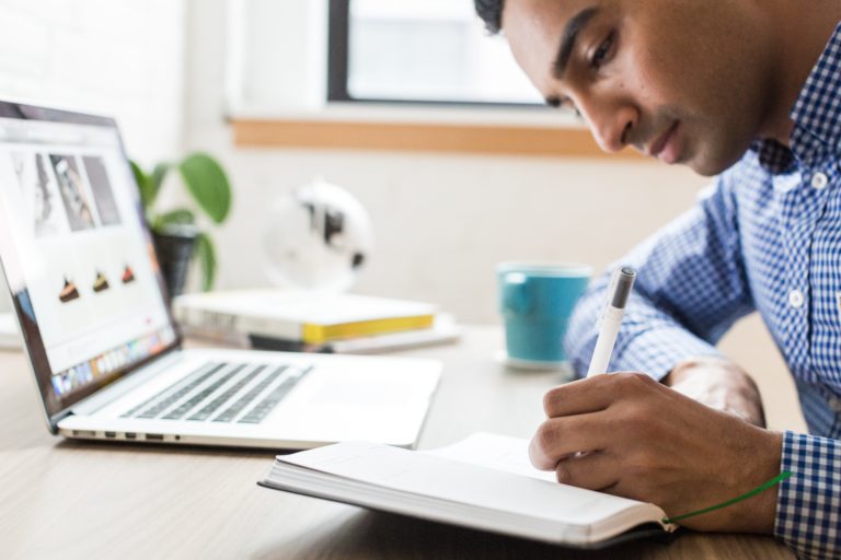 A businessman sitting at his computer, taking notes on the 10 Best Amazon Seller Blogs of 2020.