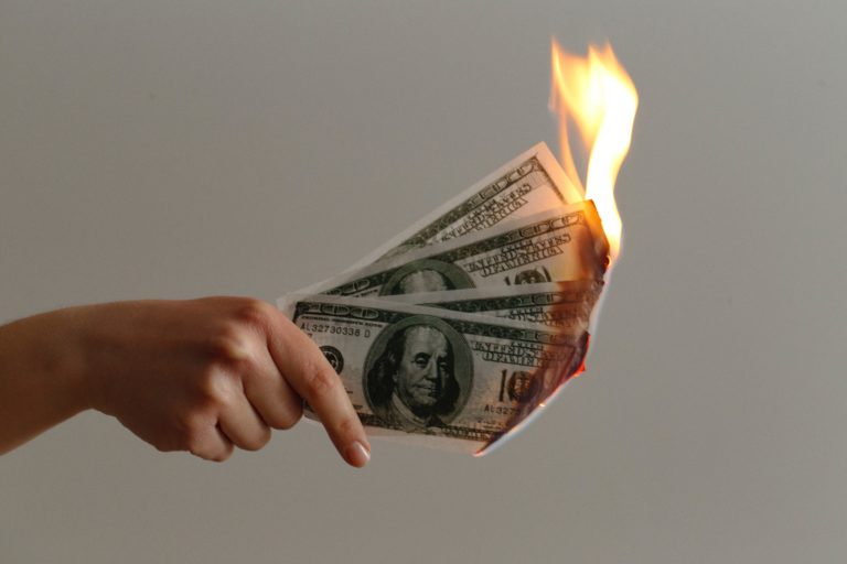 A photo of three $100 bills on fire, signifying the way that small businesses waste money.