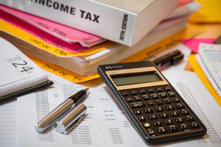 A desk with various accounting materials piled on top, including a calculator, a financial spreadsheet, and a book about income tax.