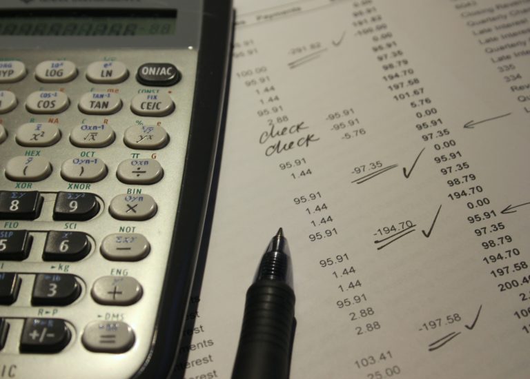 A calculator placed on top of a sheet listing a bunch of transactions.