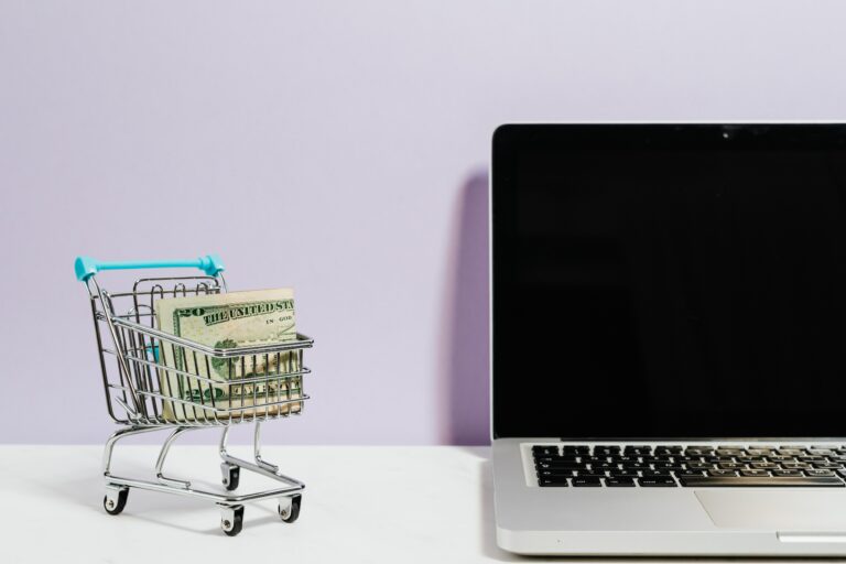 A mini shopping cart with money in it pictured next to a computer. The image signifies how to turn around a failing e-commerce business.