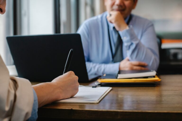 A business owner asking a bookkeeper a series of questions and writing down the answers.